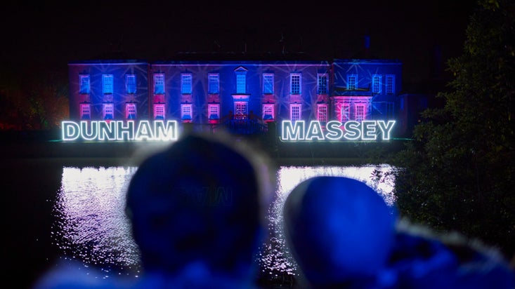 A couple gaze at the house illuminated in festive lights at Christmas at Dunham Massey, Cheshire.